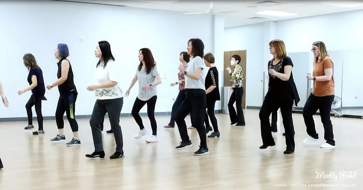 Women in a dance studio practicing a synchronized routine on a wooden floor.