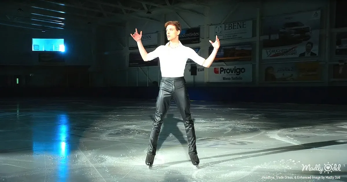 A figure skater in a white shirt and black pants stands gracefully on ice, arms outstretched.