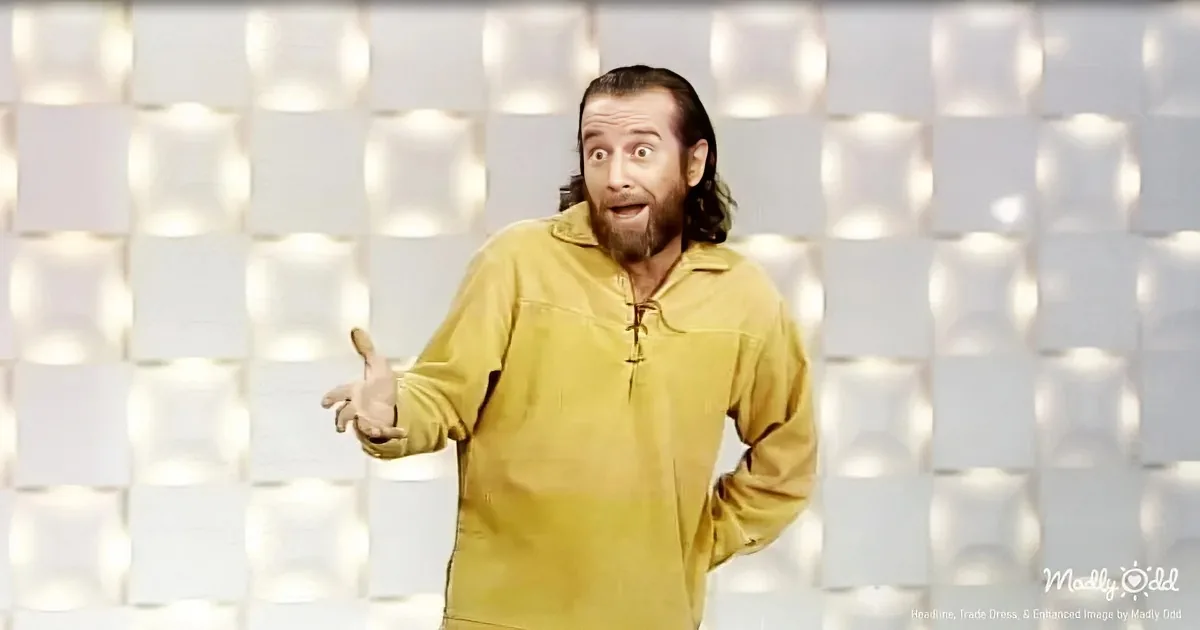 A man in a yellow shirt stands with an open mouth, gesturing with his hands against a light, geometric background.