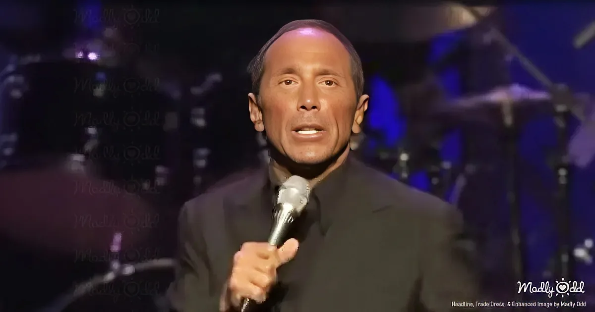A man in a black suit holds a microphone, singing on stage with a band in the background.