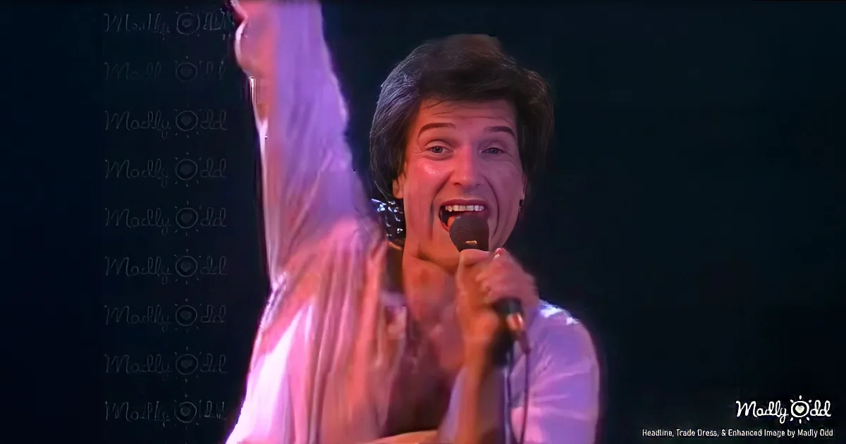 A person singing into a microphone, wearing a white shirt, with a dark background and a watermark.