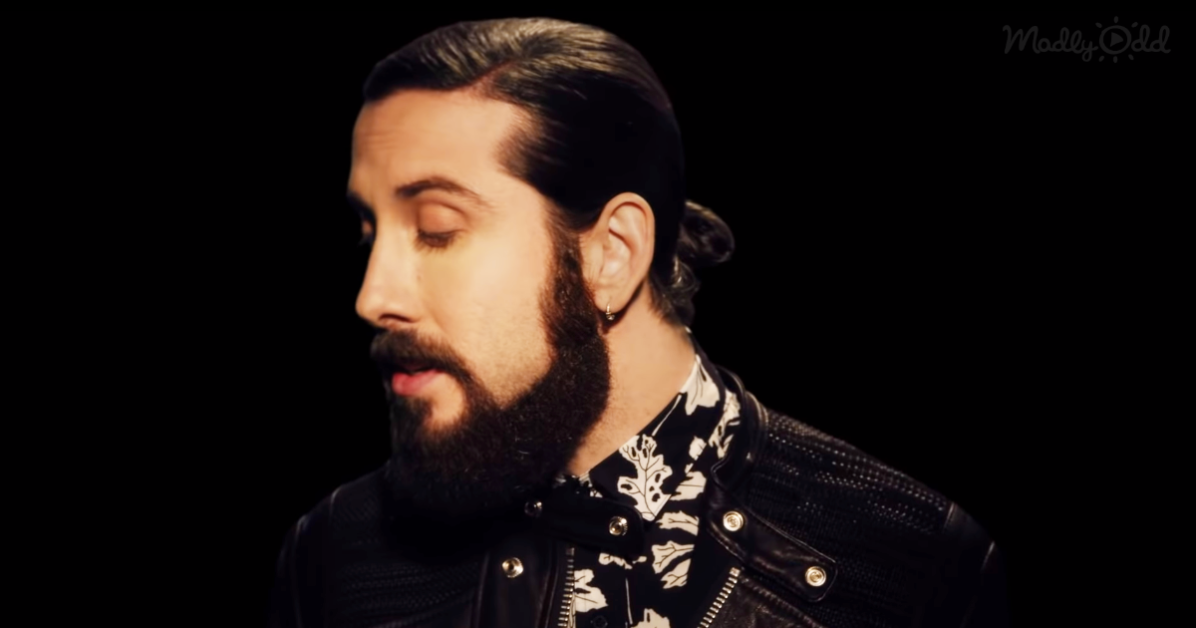 A man with a beard and ponytail, wearing a black leather jacket and a floral shirt, is captured in profile against a dark...