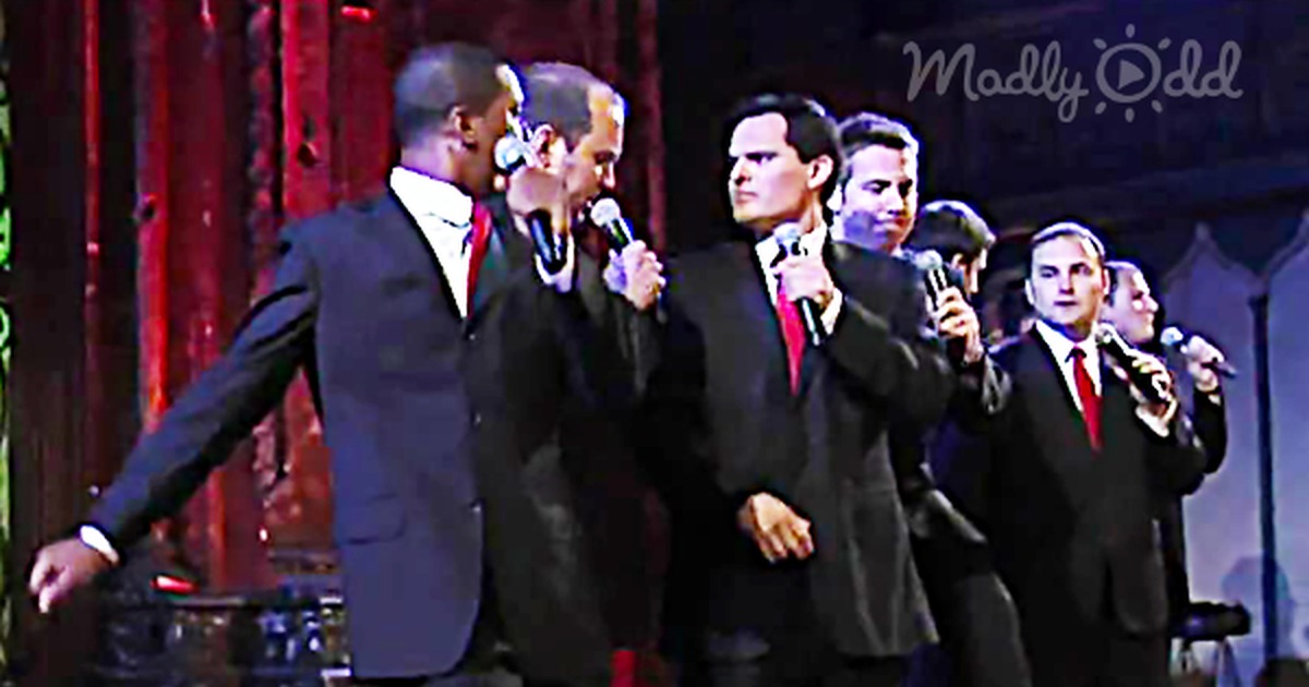 A group of men in suits performs "Christmas Can-Can" with a humorous dance, making the audience laugh.