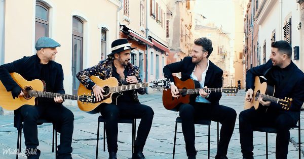 The '40 Fingers' guitar quartet seated closely, playing acoustic guitars in a synchronized performance of a Michael Jackson medley.