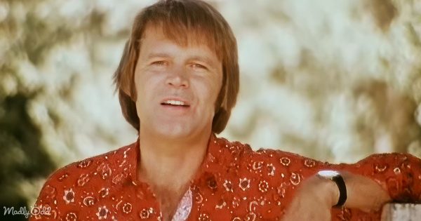 Glen Campbell clad in a cowboy outfit, spotlight highlighting his presence in the 'Rhinestone Cowboy' music video.