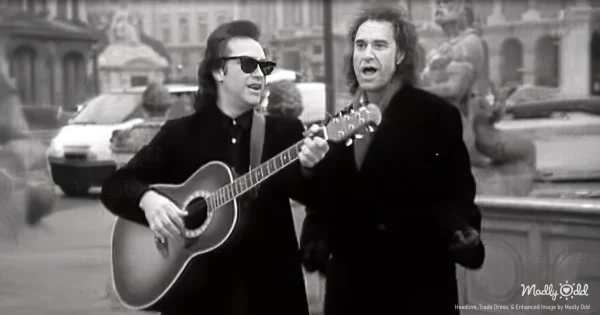 The Kinks stand on a dimly lit stage in 1993, Ray Davies with a microphone in hand, passionately delivering the lyrics while Dave Davies rips through a guitar solo, bathed in a soft blue spotlight, channeling vintage Roy Orbison energy.